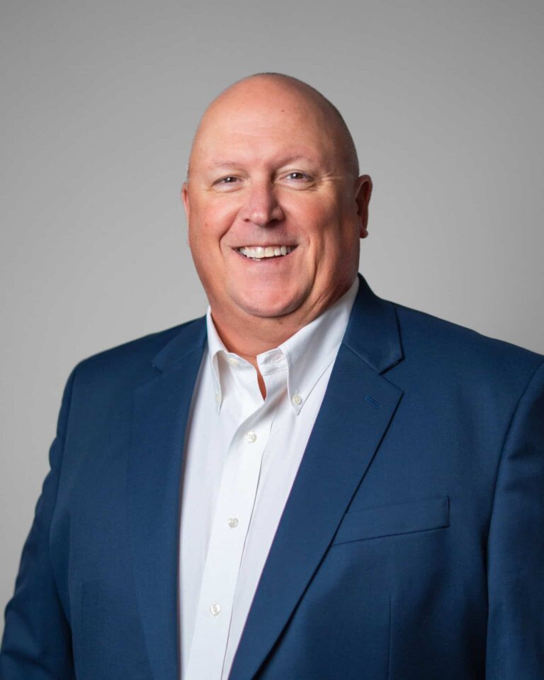 Smiling man in a blue suit, representing Asset Enterprises' mission to enhance and sustain critical retail technology.