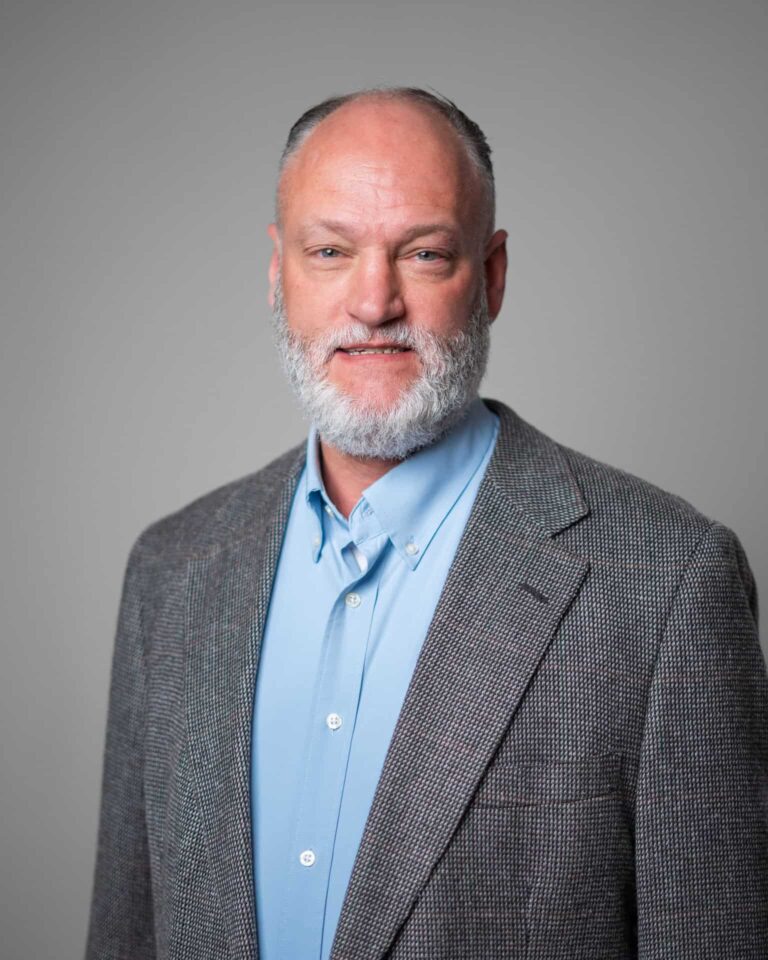 Business executive in a grey blazer and blue shirt, representing Asset Enterprises' mission and values.