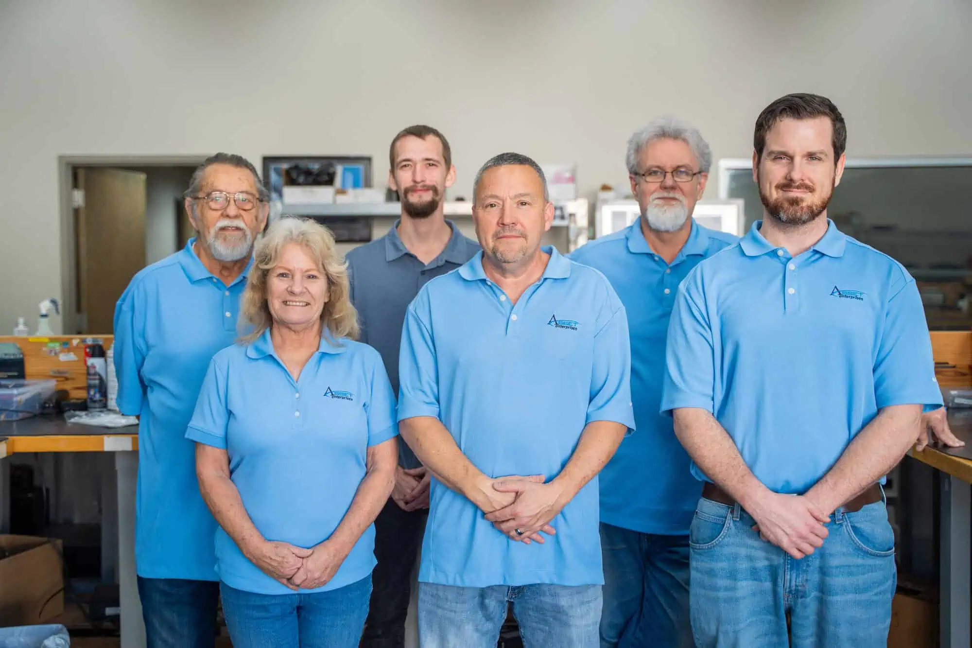 Team of six smiling employees in blue shirts at Asset Enterprises, experienced in depot maintenance.