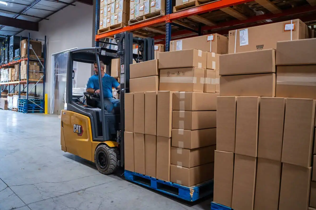Forklift transporting stacked boxes in a warehouse, highlighting site maintenance and store level speed consistency.