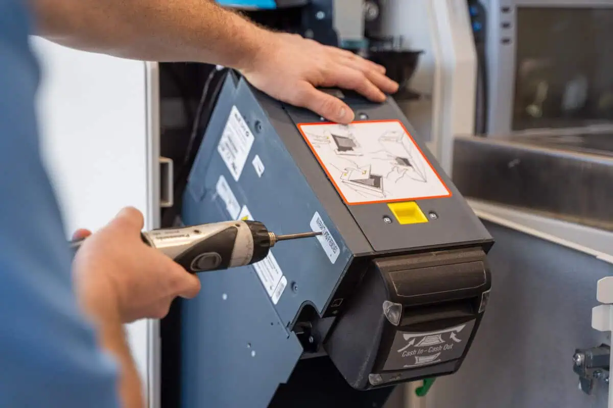 Technician with drill de-installs cash unit, demonstrating where discipline matters most to avoid costly mistakes.