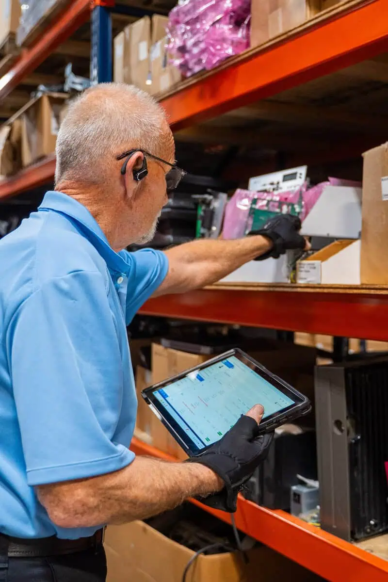 Man in warehouse using a tablet for inventory management, exemplifying services every environment and full lifecycle tech support.